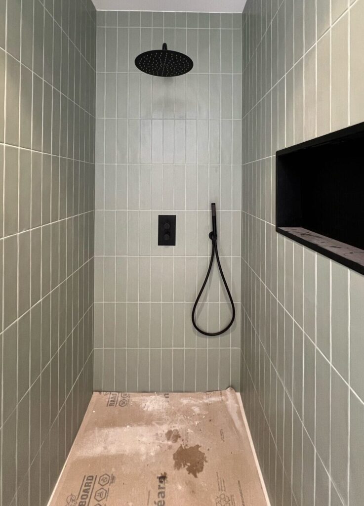 Douche rénovée avec carrelage vert vertical, robinetterie noire encastrée et niche murale