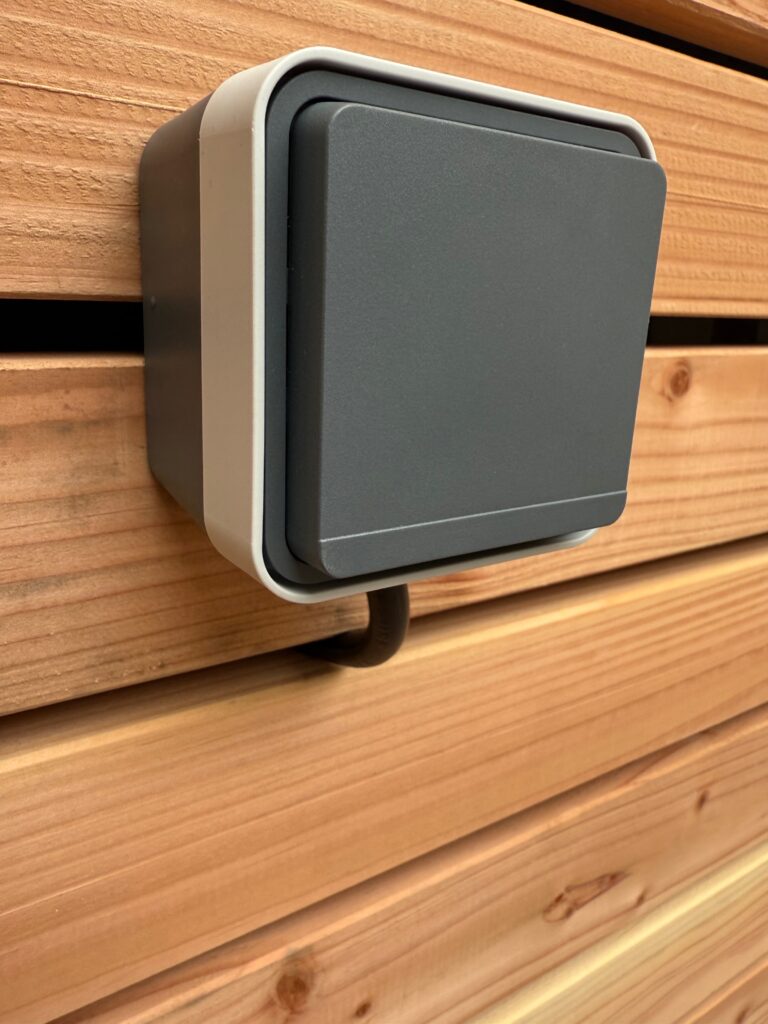 Interrupteur étanche posé sur un bardage en bois à l’extérieur de la maison.