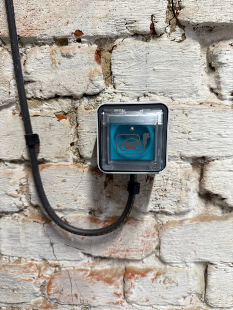 Prise de recharge pour véhicule électrique installée sur un mur de briques extérieur.