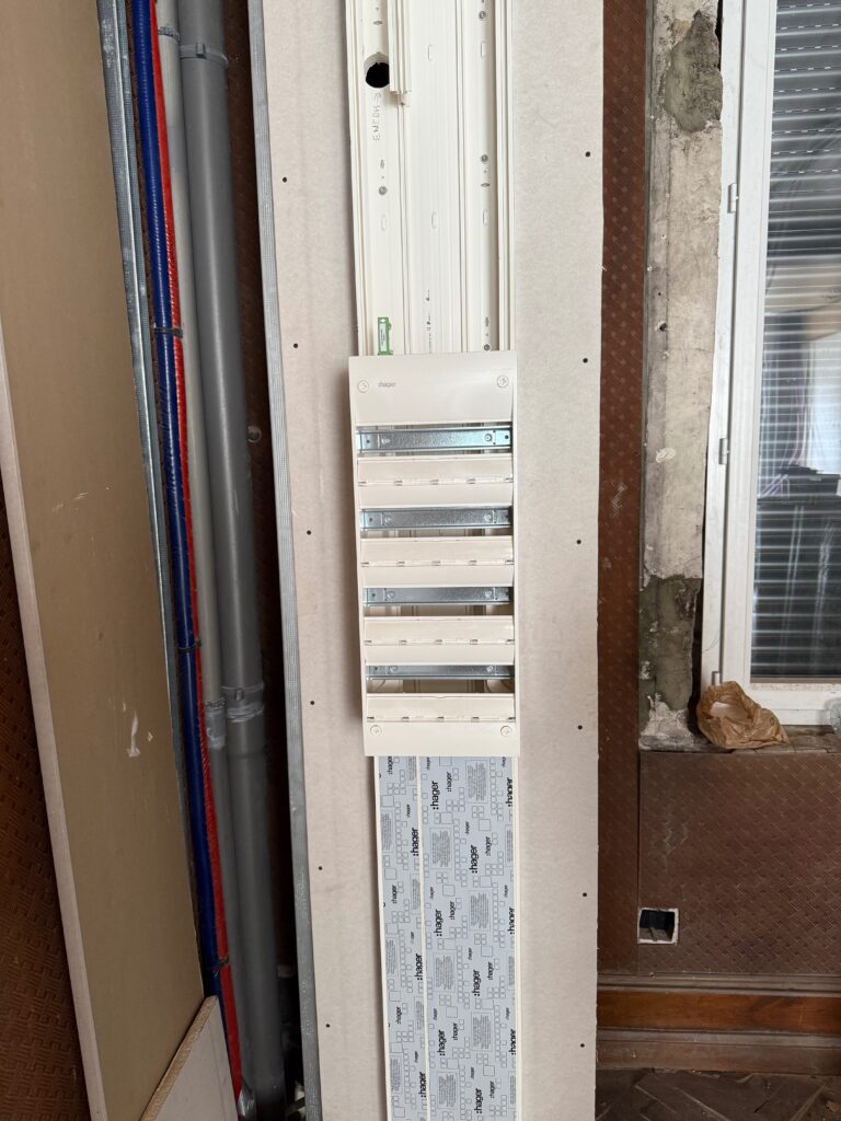 Tableau électrique encastré dans une cloison en cours de rénovation, avec les arrivées de câbles apparentes.