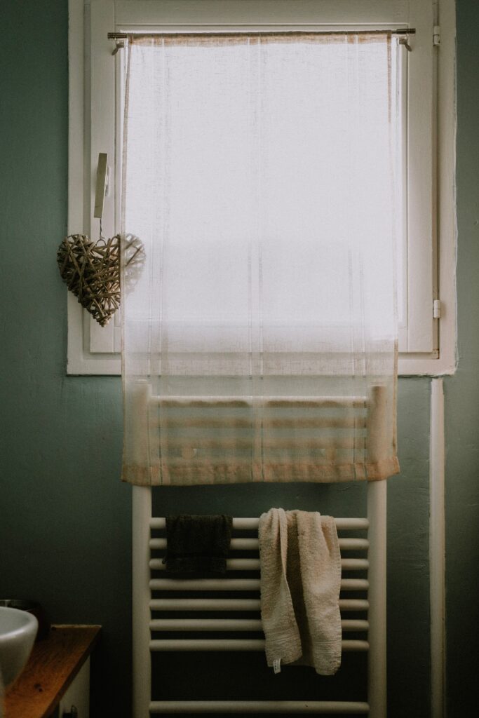 Radiateur sèche-serviettes blanc installé sous une fenêtre de salle de bain